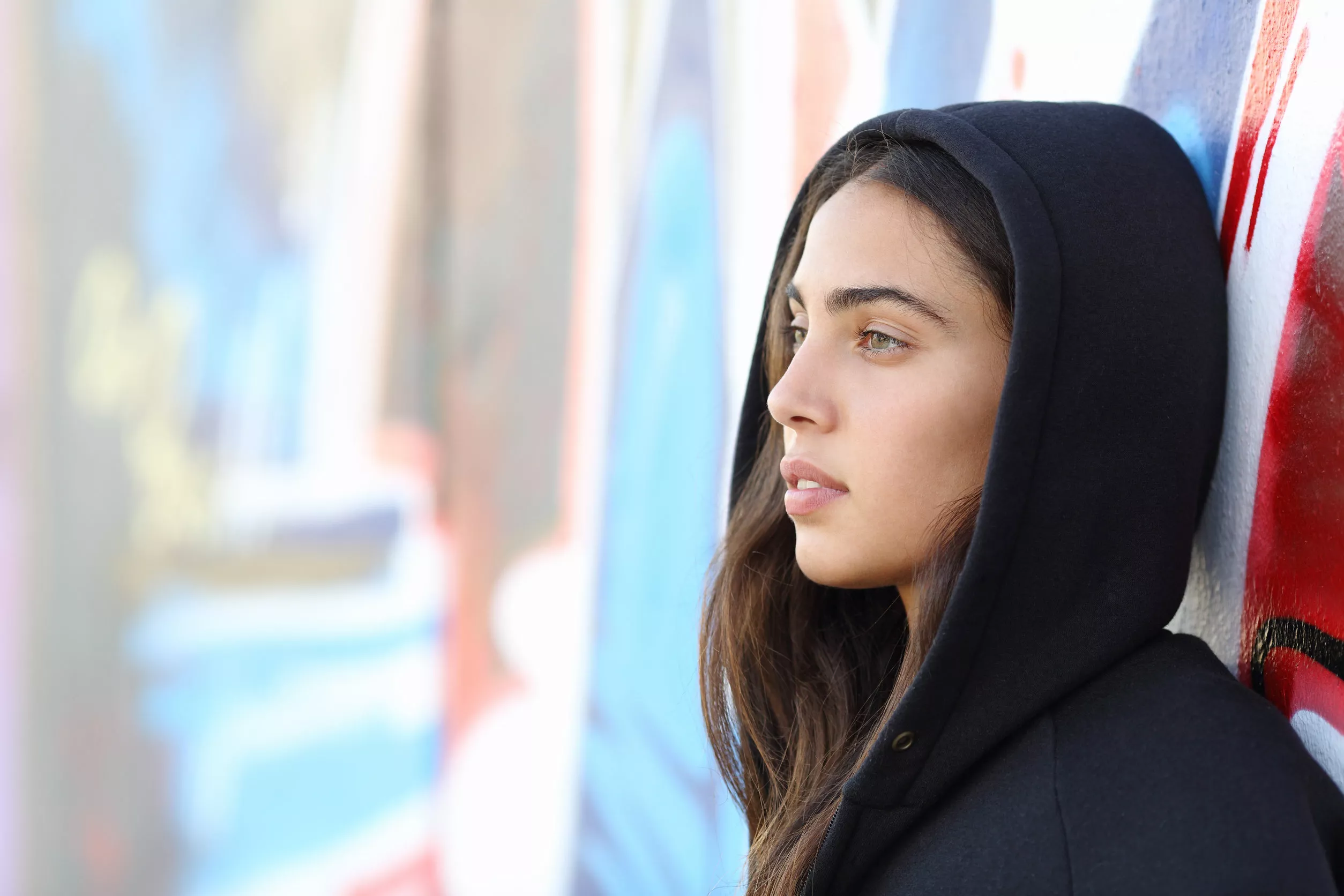 Troubled teenage girl leans on a graffiti-painted wall.